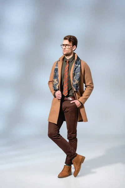 Lunghezza intera di uomo alla moda in cappotto invernale e stivali in piedi con mano in tasca su grigio — Foto stock