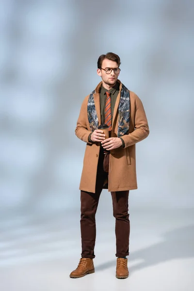 Pleine longueur de l'homme élégant en manteau d'hiver tenant tasse en papier sur gris — Photo de stock