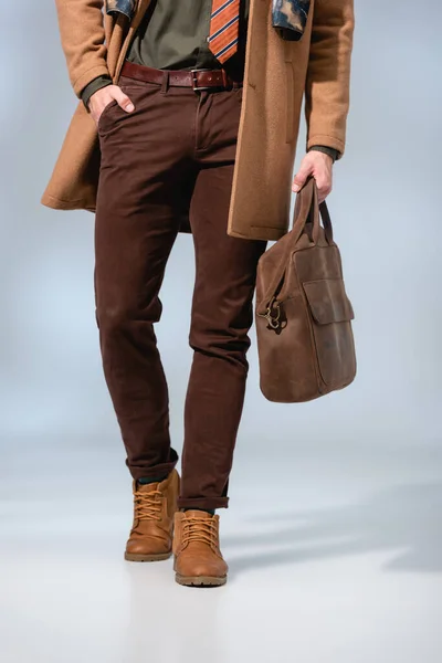 Abgeschnittene Ansicht des stilvollen Mannes mit Lederaktentasche und mit der Hand in der Tasche auf grau stehend — Stockfoto