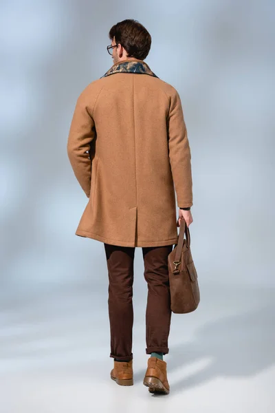 Vue arrière de l'homme élégant en manteau d'hiver tenant la mallette en cuir sur gris — Photo de stock