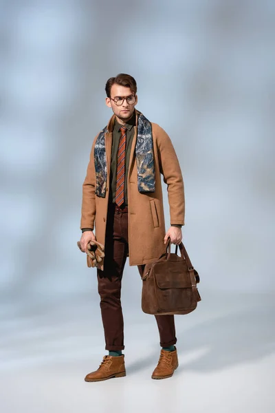 Comprimento total do homem elegante no casaco de inverno segurando pasta de couro e luvas em cinza — Fotografia de Stock