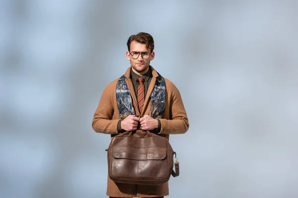 Стильный мужчина в зимнем пальто с коричневым портфелем на сером — стоковое фото