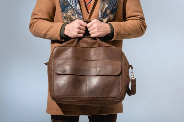 Обрезанный вид стильного человека в зимнем пальто с кожаным портфелем, изолированным на сером — стоковое фото
