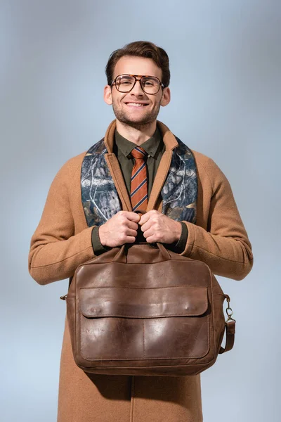 Cheerful man in winter coat holding leather briefcase on grey — Stock Photo