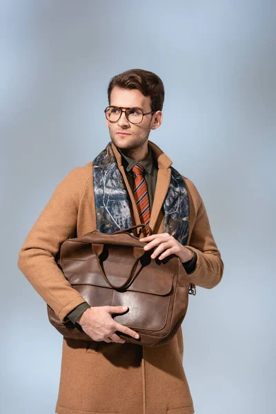 Trendy man in winter coat holding brown briefcase on grey — Stock Photo