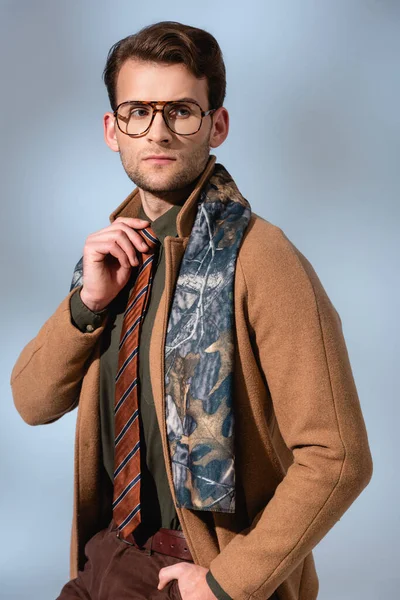 Trendy man in winter coat and glasses adjusting tie on grey — Stock Photo