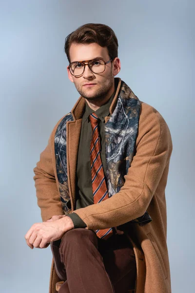 Elegante uomo in abito invernale e bicchieri seduto sulla sedia su grigio — Foto stock