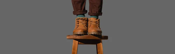 Abgeschnittene Ansicht eines Mannes in Stiefeln, der auf einem Holzstuhl steht, isoliert auf grau, Banner — Stockfoto