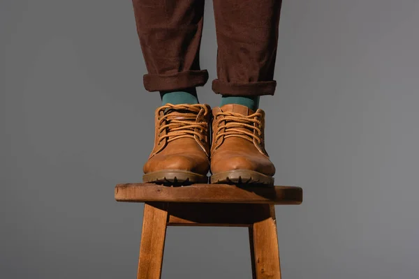 Cropped view of man in boots standing on wooden chair isolated on grey — Stock Photo