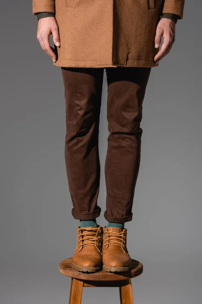 Partial view of man in boots standing on wooden chair isolated on grey — Stock Photo