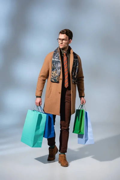 Full length of trendy customer in glasses holding paper bags on grey — Stock Photo