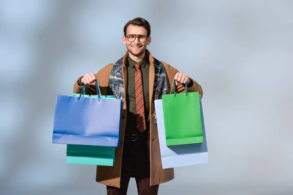 Cliente positivo en gafas con bolsas de papel en gris - foto de stock