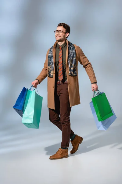 Full length of smiling customer in glasses holding paper bags on grey — Stock Photo