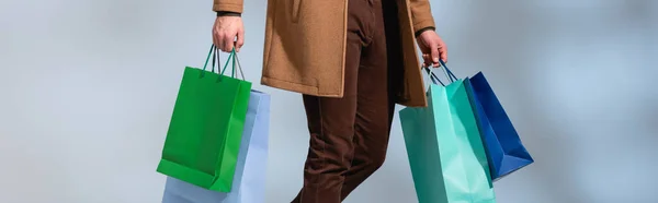 Vista parcial del cliente en abrigo de invierno sosteniendo bolsas de papel aisladas en gris, pancarta - foto de stock