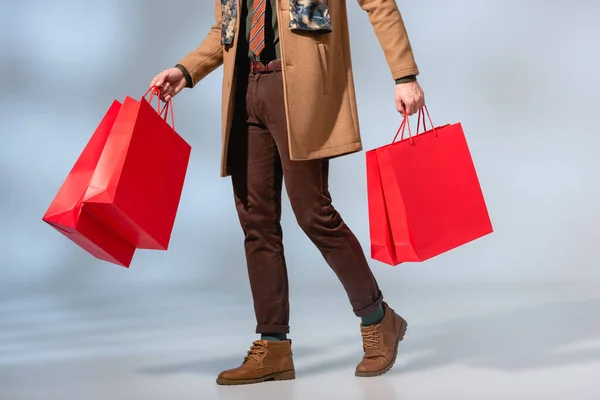 Teilansicht des Kunden im Mantel mit Papiertüten auf grau — Stockfoto