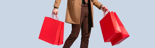 Vista parcial del cliente en abrigo sosteniendo bolsas de papel aisladas en gris, banner - foto de stock