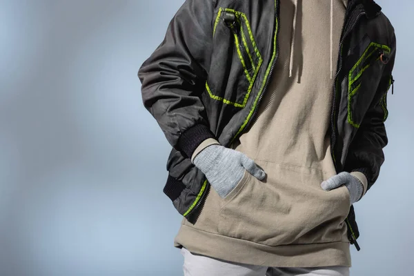 Cropped view of man in anorak and gloves standing with hands in pockets on grey — Stock Photo