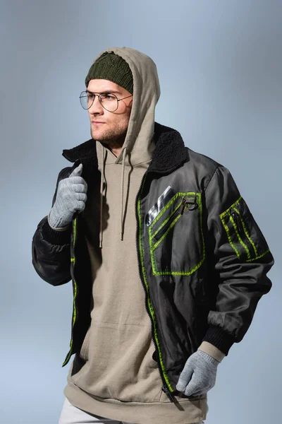 Fashionable man in glasses, hat, anorak and gloves isolated on grey — Stock Photo