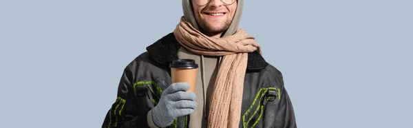 Partial view of cheerful man in hat, hoodie and anorak holding paper cup isolated on grey, banner — Stock Photo
