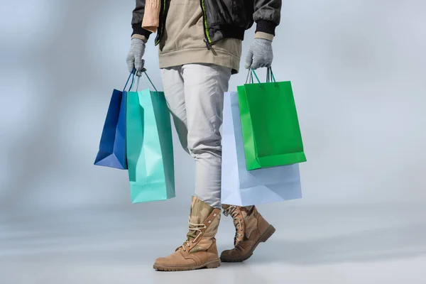 Vista ritagliata dell'uomo elegante in abito invernale che tiene borse della spesa sul grigio — Foto stock