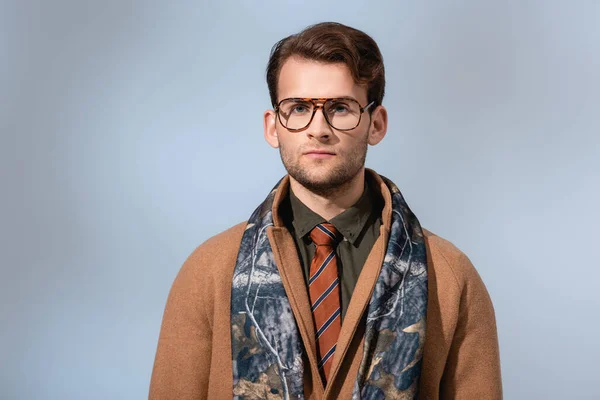 Trendy man in glasses and winter coat looking at camera on grey — Stock Photo