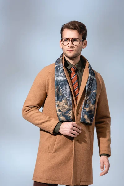 Trendy man in glasses, scarf and winter coat looking away on grey — Stock Photo