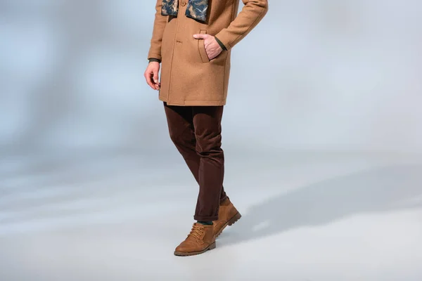 Cropped view of man in winter coat and boots standing with hand in pocket on grey — Stock Photo