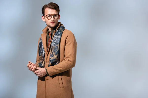 Fashionable man in glasses, scarf and winter coat looking away on grey — Stock Photo