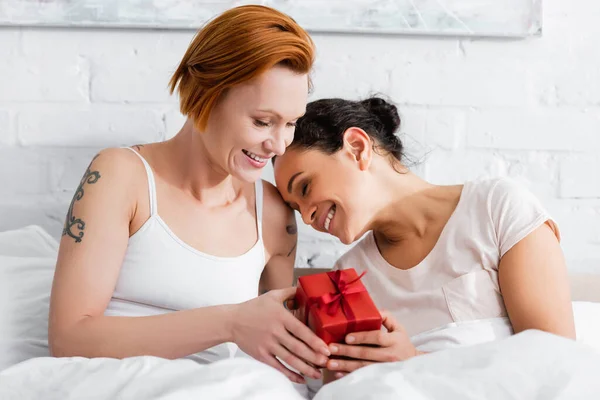 Redhead woman presenting gift to african american girlfriend on valentines day — Stock Photo