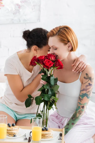 Africano americano mujer abrazando lesbiana novia holding rojo rosas en habitación - foto de stock