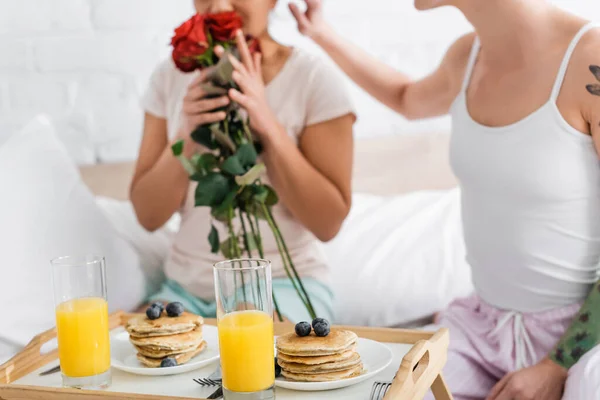 Abgeschnittene Ansicht einer lesbischen Frau, die rote Rosen in der Nähe von Freundin und Frühstück im Bett riecht — Stockfoto