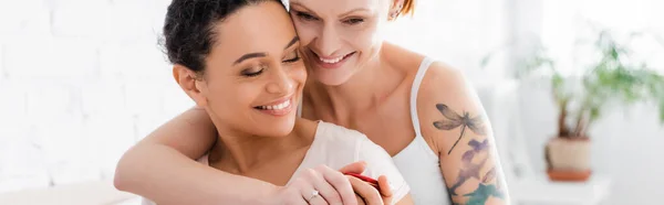 Heureuse femme tatouée avec bague de mariage sur le doigt embrassant africaine américaine lesbienne copine, bannière — Photo de stock