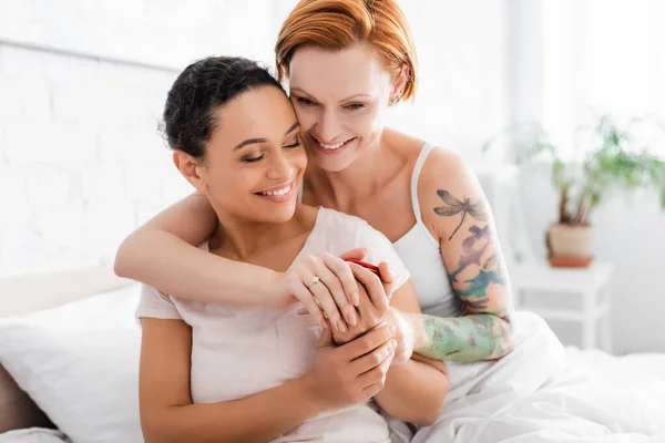 Happy redhead lesbian woman with wedding ring on finger embracing african american girlfriend holding jewelry box — Stock Photo