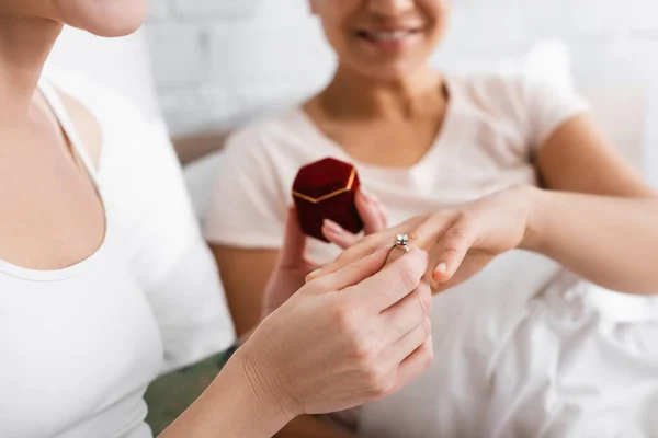 Vista recortada de la mujer lesbiana poniendo anillo en el dedo de la novia afroamericana al hacer la propuesta de boda, fondo borroso - foto de stock