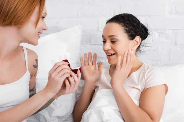 Étonné femme afro-américaine geste près petite amie lesbienne tenant boîte à bijoux tout en faisant la demande en mariage — Photo de stock