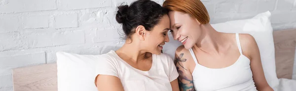 Весела міжрасова лесбіянка пара сміється обличчям до обличчя в ліжку, банер — стокове фото