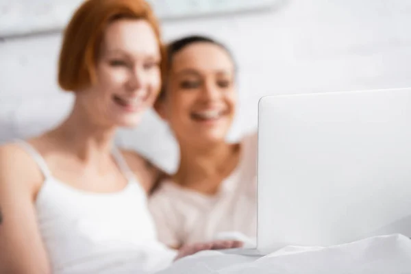 Вибірковий фокус ноутбука біля веселої міжрасової лесбійської пари дивитися фільм в ліжку — стокове фото