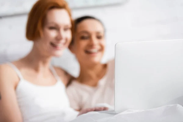 Enfoque selectivo de la computadora portátil cerca alegre interracial lesbianas pareja viendo película en la cama - foto de stock
