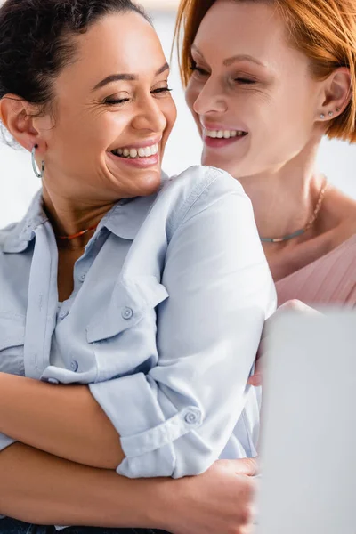 Excité afro-américaine femme riant près gai lesbienne copine, flou au premier plan — Photo de stock