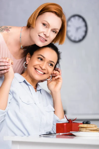 Redhead lesbian woman holding hands of happy african american girlfriend on valentines day, blurred foreground — Stock Photo