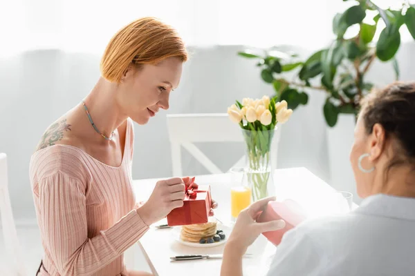 Interracial lesbian couple holding gift boxes during breakfast on valentines day — Stock Photo