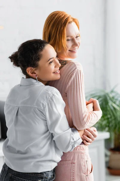 Glücklich afrikanisch amerikanisch frau umarmt rotschopf lesbische freundin zu Hause — Stockfoto