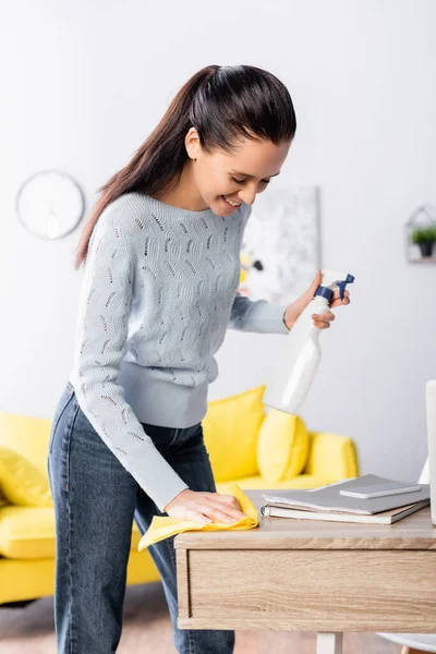 Young housewife holding detergent spray and wiping table with rag — Stock Photo