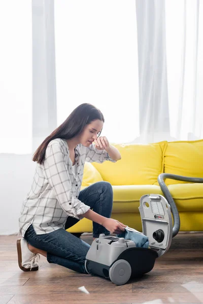 Mujer alérgica limpiando la nariz mientras cambia la bolsa de polvo en la aspiradora - foto de stock