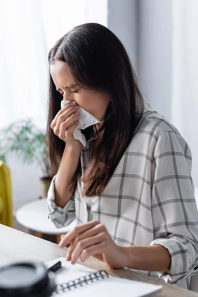 Junge Frau wischt sich Nase mit Papierserviette ab, während sie an Allergie auf verschwommenem Vordergrund leidet — Stockfoto