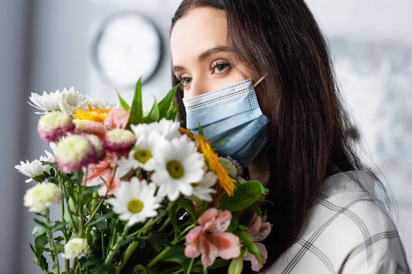 Junge allergische Frau in medizinischer Maske mit Blumenstrauß zu Hause — Stockfoto