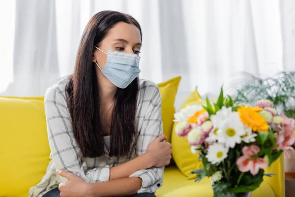 Triste donna allergica in maschera medica seduta vicino ai fiori a casa — Foto stock