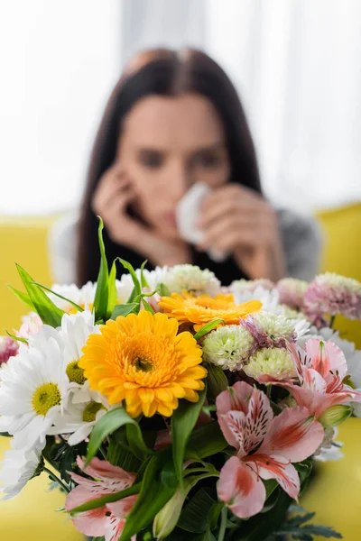 Foco seletivo de flores perto de mulher que sofre de alergia em fundo turvo — Fotografia de Stock