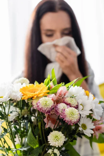 Selective focus of bouquet near allergic woman wiping nose with paper napkin on blurred background — Stock Photo