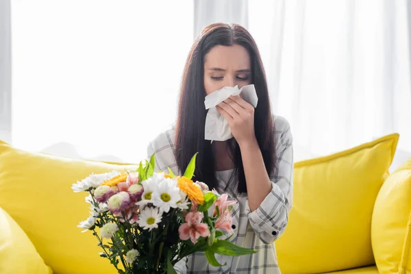 Allergische Frau wischt sich Nase mit Papierserviette ab, während sie neben Blumen sitzt — Stockfoto